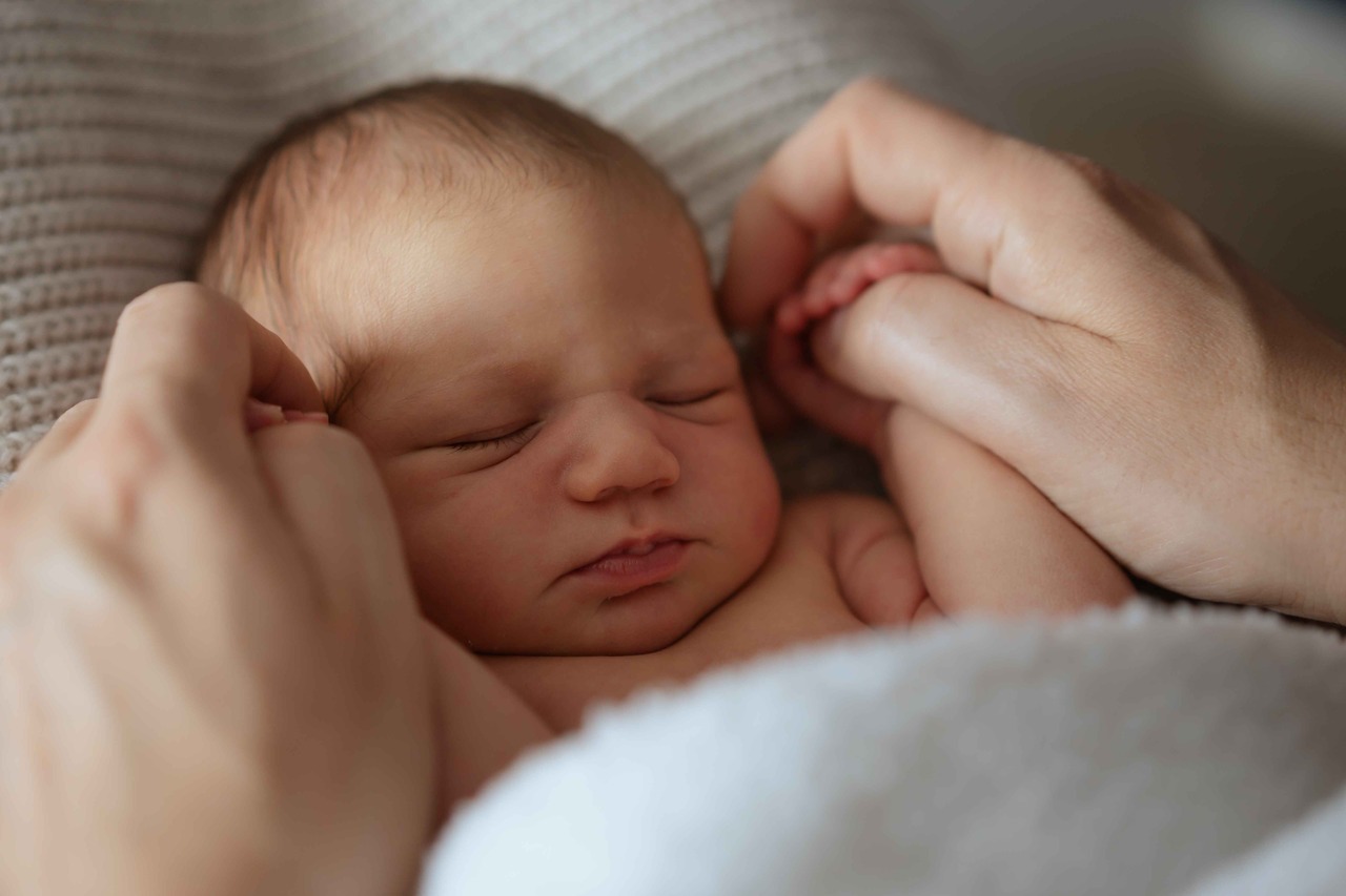 Iemand heeft de handjes van een slapende baby vast